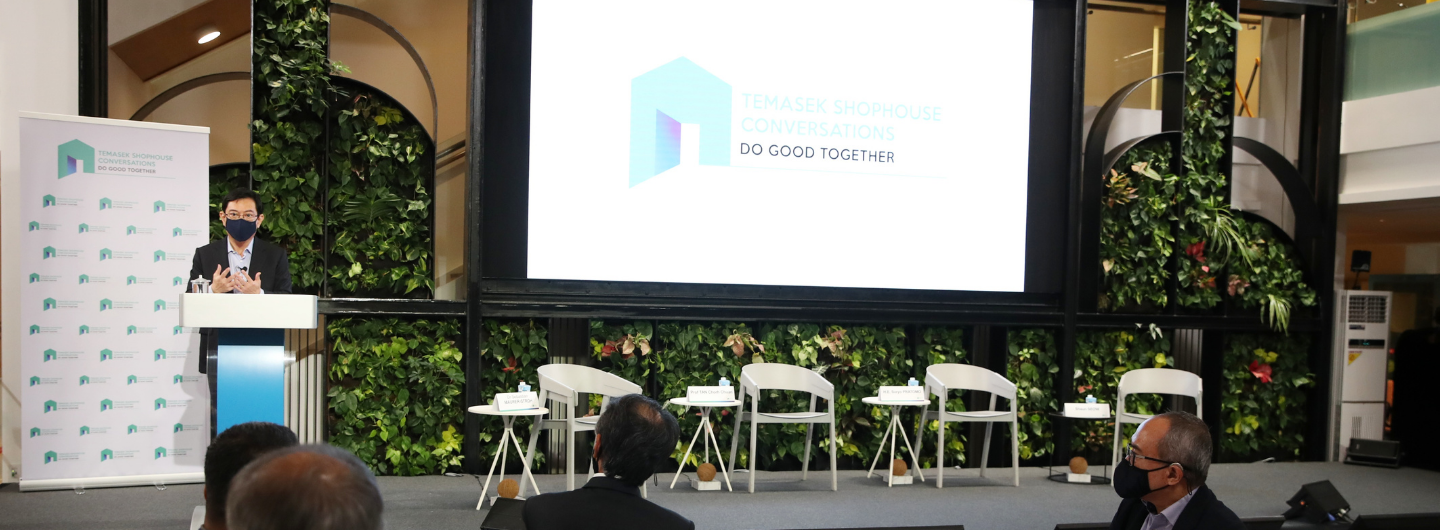 Speaker at Temasek Shophouse Conversations in front of an audience, with a screen and a plant wall.